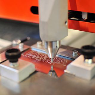 Igła znakowarki wykonująca mikropunktowe grawerowanie na metalowej płytce.